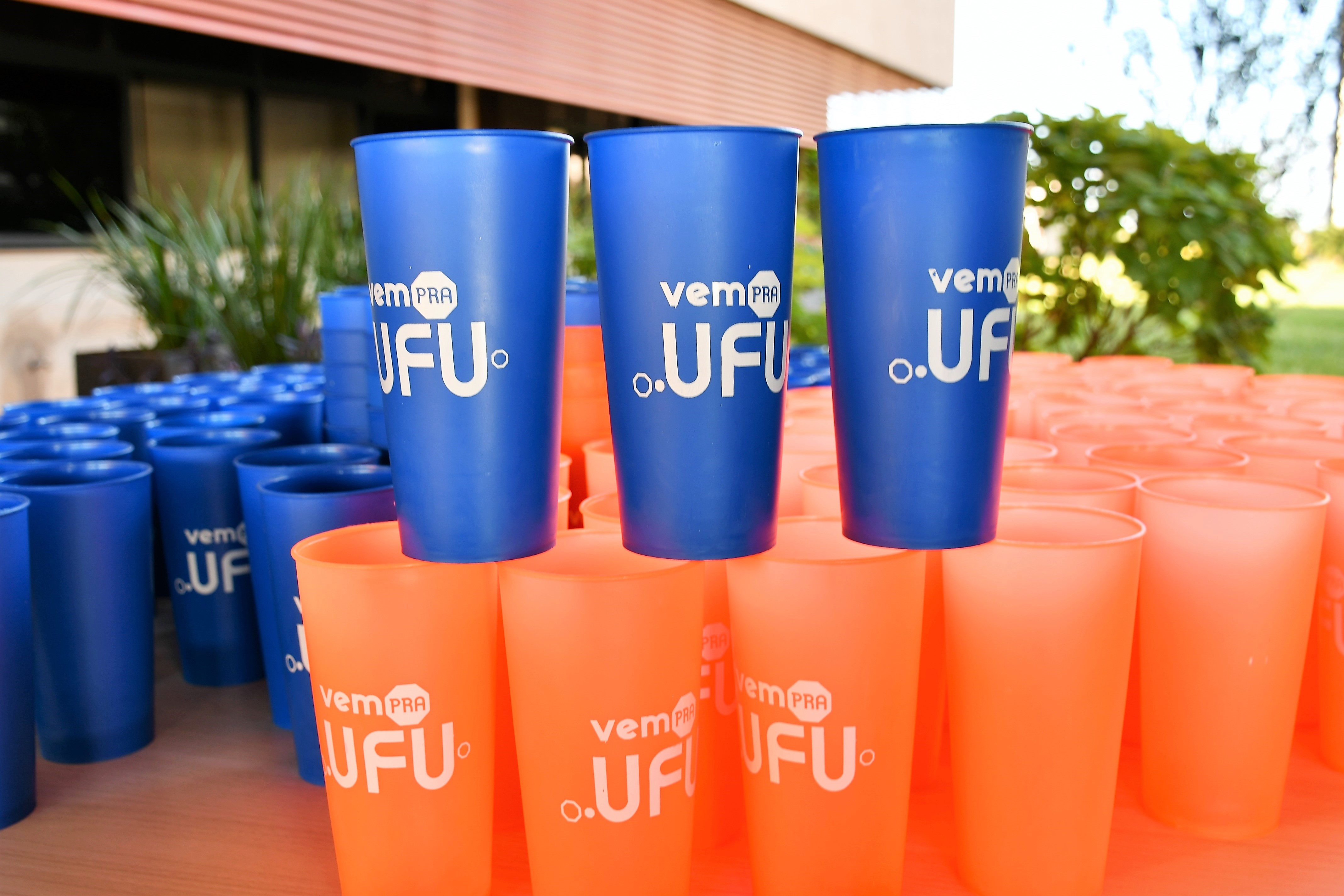 Imagem de copos de plástico azuis e alaranjados estilizados com a logo do evento