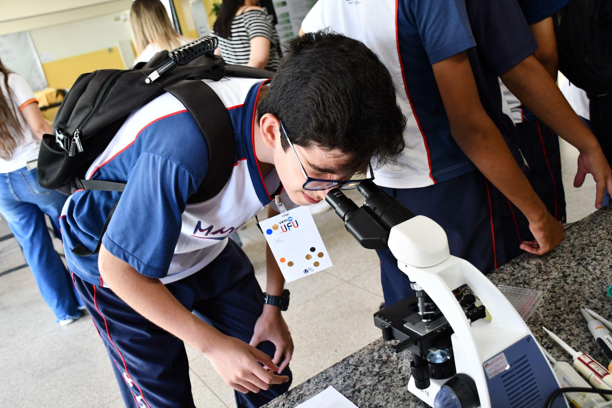 Estudante do ensino médio com os olhos num microscópio óptico